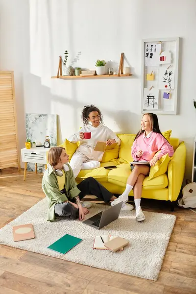 Eine bunte Gruppe von Freunden, darunter gemischtrassige Teenager-Mädchen, sitzt zusammen auf einer leuchtend gelben Couch, plaudert und studiert.. — Stockfoto