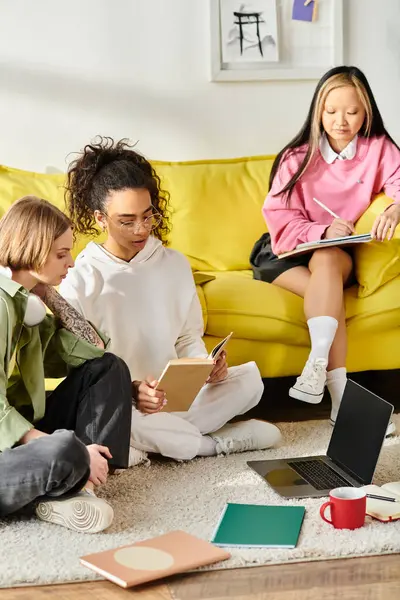 Diverse Teenager-Mädchen sitzen auf dem Boden neben der gelben Couch, lernen zusammen und bauen durch gemeinsame Bildung Freundschaft auf. — Stockfoto