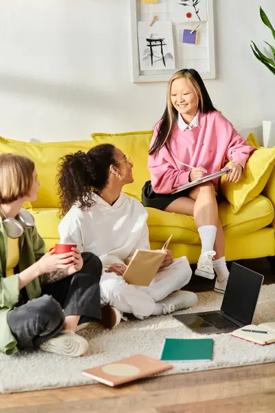 Un variegato gruppo di ragazze adolescenti studia e chiacchiera insieme su un vibrante divano giallo, creando una scena calda e invitante. — Foto stock