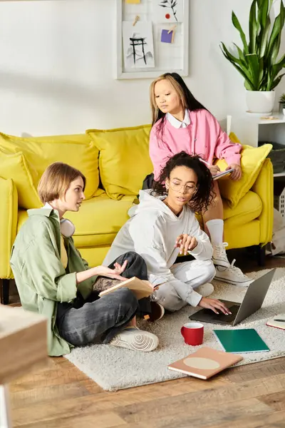 Diverse teenage girls in deep study, seated on the floor in front of a vibrant yellow couch, surrounded by books and papers. — Stock Photo
