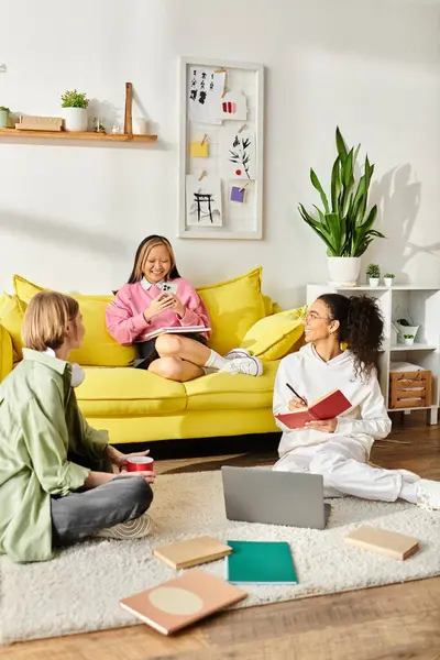 Un grupo diverso de mujeres charlando y estudiando en un vibrante sofá amarillo en una acogedora habitación. - foto de stock