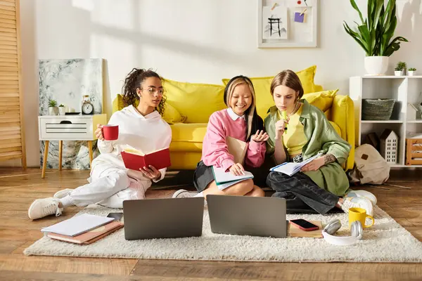 Tres mujeres jóvenes, que representan diferentes razas, trabajan juntas en computadoras portátiles en un entorno acogedor, encarnando la amistad y la dedicación a la educación. - foto de stock