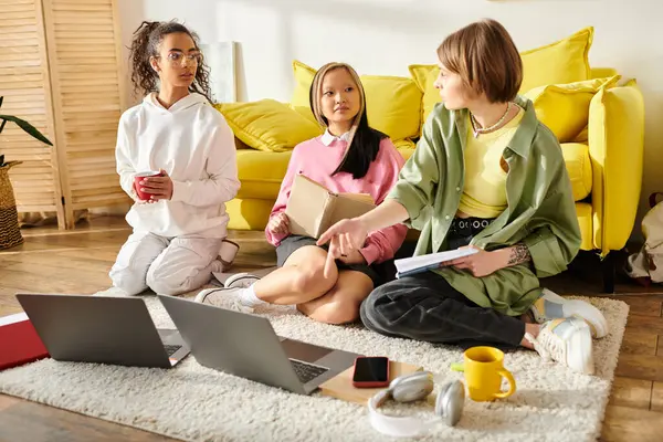 Grupo de adolescentes de diversos orígenes que estudian juntas en casa, absortas en sus computadoras portátiles. - foto de stock