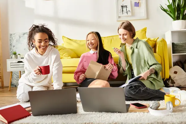 Три дівчинки-підлітки різних рас сидять на підлозі з ноутбуками, заглиблюючись у навчання і сприяючи зв'язку дружби через освіту. — стокове фото
