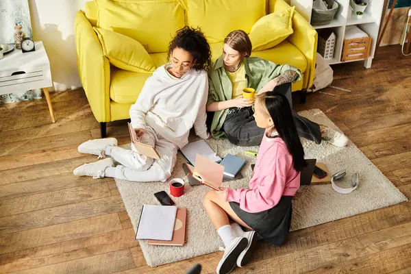 A group of interracial teenage girls sitting on the floor, studying together next to a bright yellow couch. — Stock Photo