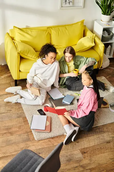 Three young girls of different races sitting on the floor immersed in books, studying together at home in a display of friendship and dedication to education. — Stock Photo