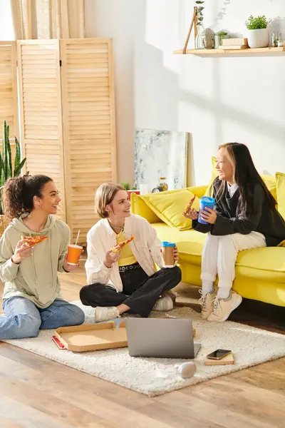 Un grupo de diversas adolescentes sentadas en el suelo, compartiendo risas y rebanadas de pizza en un acogedor entorno hogareño. - foto de stock