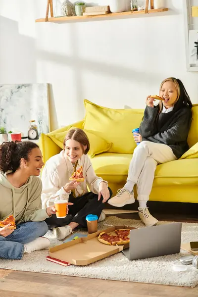 Багатокультурні дівчата-підлітки збираються на підлозі, їдять піцу та діляться сміхом вдома. — стокове фото