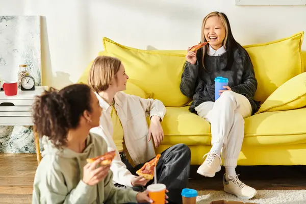 Разнообразная группа девочек-подростков, наслаждающихся компанией друг друга, сидя на ярком желтом диване дома. — стоковое фото