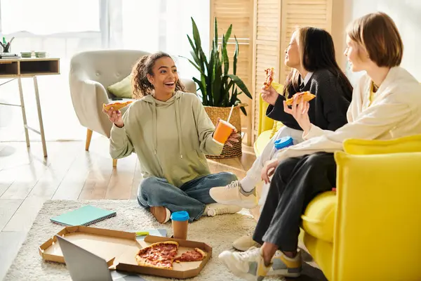 Adolescentes multiculturales se reúnen en una acogedora sala de estar, se unen sobre rebanadas de pizza y comparten la risa. - foto de stock