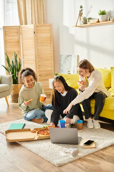 Les adolescentes de différentes races s'assoient ensemble sur le sol, riant et mangeant de la pizza, profitant d'un moment d'amitié. — Photo de stock
