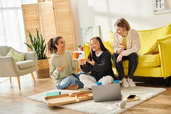 Un groupe diversifié d'adolescentes assises sur le sol, dégustant une pizza ensemble dans un cadre confortable à la maison. — Photo de stock
