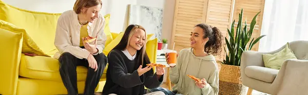 Diverse group of teenage girls chatting and laughing while sitting together on a vibrant yellow couch at home. — Stock Photo