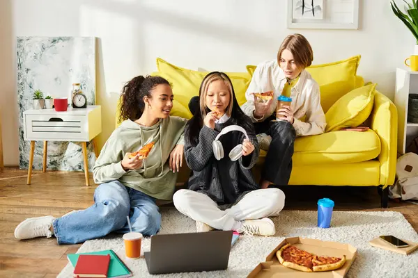 Tres adolescentes diversas sentadas juntas en el suelo, disfrutando de una comida de pizza. - foto de stock