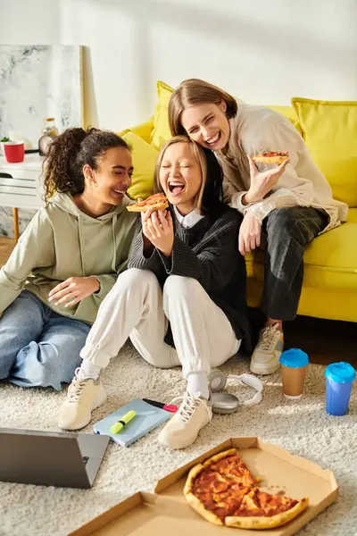 Un grupo diverso de adolescentes sentadas en el suelo, disfrutando de la pizza y construyendo amistad en casa. - foto de stock