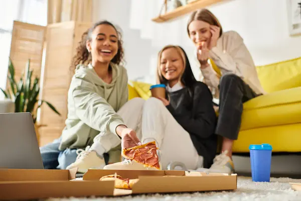 Groupe diversifié d'adolescentes profitant d'un lieu de rencontre décontracté, assises sur le sol et savourant des tranches de pizza ensemble. — Photo de stock