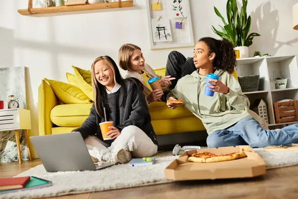 Tres adolescentes interracial se sientan en el suelo, disfrutando de pizza y café en un ambiente acogedor en casa. - foto de stock