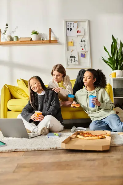 Grupo de chicas adolescentes de diferentes razas compartiendo risas y pizza mientras se sientan juntas en un acogedor sofá. - foto de stock