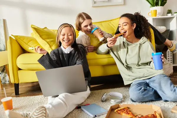 Des adolescentes multiculturelles s'assoient sur le sol, participent à des activités numériques sur leur ordinateur portable et partagent des intérêts communs.. — Photo de stock
