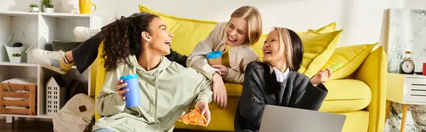 Разнообразная группа девочек-подростков, разных рас, сидящих вместе на ярко-желтом диване, улыбающихся и болтающих, демонстрирующих красоту дружбы. — стоковое фото