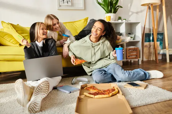 Groupe diversifié d'adolescentes assises ensemble sur le sol, profitant de tranches de pizza dans un cadre confortable à la maison. — Photo de stock