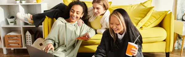 Interracial teenage girls enjoying friendship on a yellow couch while sitting and chatting at home. — Stock Photo