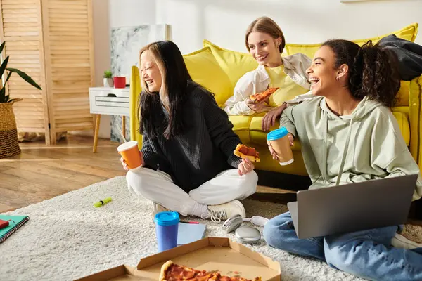 Un grupo diverso de adolescentes se sientan alegremente en el suelo, comiendo pizza juntas en un ambiente acogedor. - foto de stock