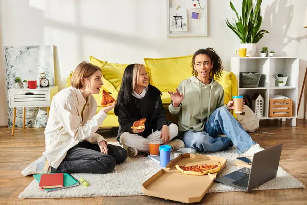 Un grupo diverso de adolescentes se sientan en el suelo, compartiendo alegremente la pizza juntas en un ambiente acogedor en casa. - foto de stock
