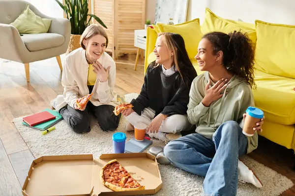 Adolescentes multiculturales sentadas en el suelo, disfrutando de la pizza juntas en un ambiente acogedor. - foto de stock