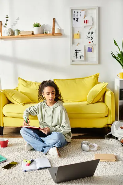 Une adolescente profondément dans le e-learning, assise sur le sol devant un canapé jaune. — Photo de stock