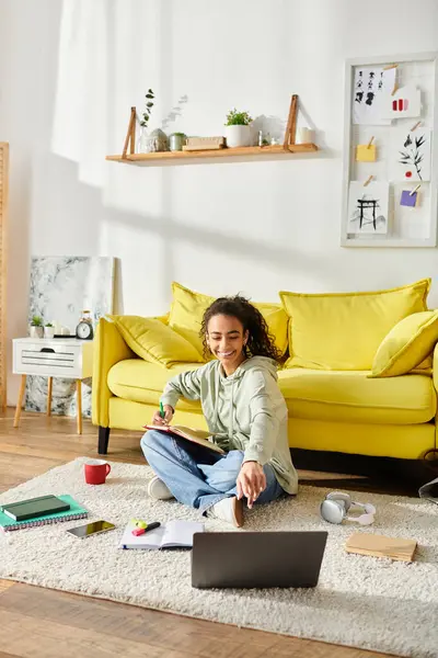 Une adolescente s'assoit sur le sol, concentrée sur son ordinateur portable pour l'apprentissage en ligne à la maison. — Photo de stock