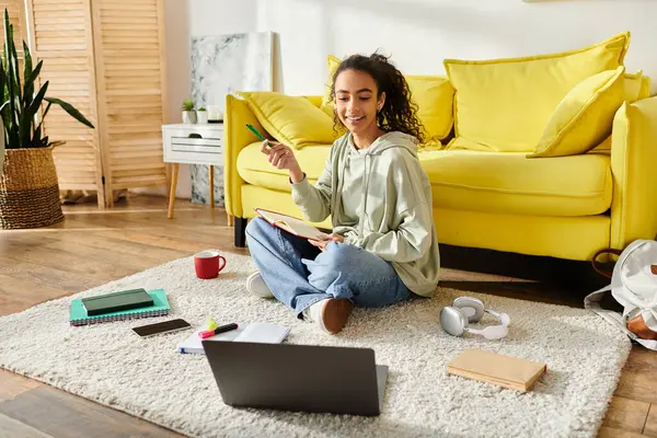 Una adolescente sentada en el suelo, totalmente centrada en su portátil, dedicada al aprendizaje electrónico en casa. - foto de stock