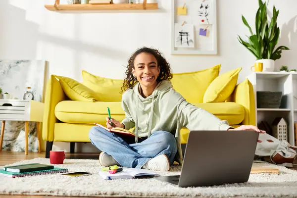 Une adolescente est assise sur le sol, concentrée sur son écran d'ordinateur portable, activement engagée dans l'apprentissage en ligne à la maison. — Photo de stock