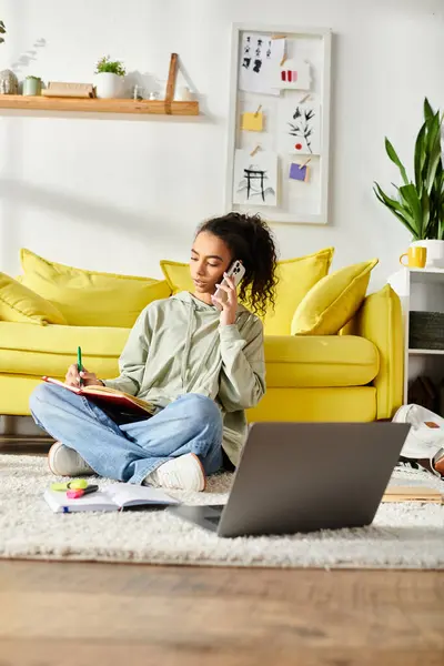 Une adolescente s'engage activement dans l'apprentissage en ligne, assise sur le sol avec un ordinateur portable tout en parlant sur son téléphone portable. — Photo de stock