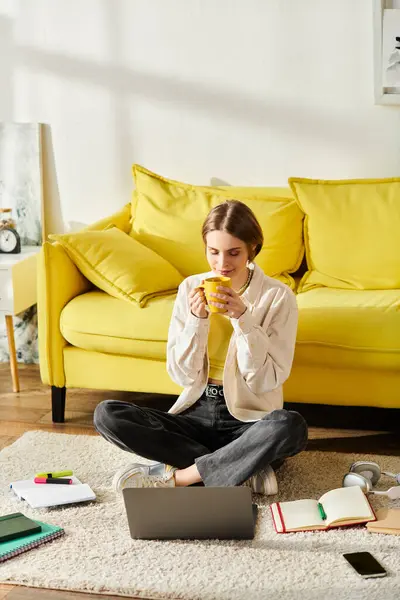 Ein Mädchen im Teenageralter sitzt mit einer Tasse Kaffee auf dem Boden, während sie zu Hause mit ihrem Laptop E-Learning betreibt. — Stockfoto