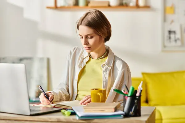 Une adolescente s'assoit à une table, étudie avec un ordinateur portable et sirote un café. — Photo de stock
