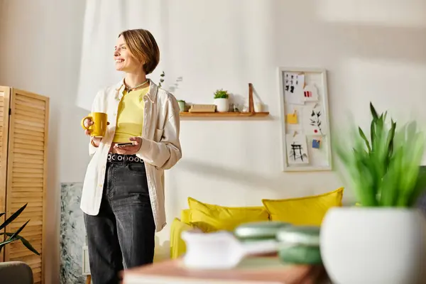 Une femme sereine se tient dans un salon ensoleillé, tenant paisiblement une tasse de café. — Photo de stock