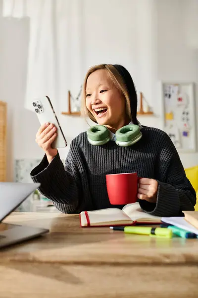 Une jeune femme asiatique s'assoit à une table, ordinateur portable ouvert, avec une tasse de café devant elle. — Photo de stock