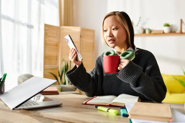 Une jeune femme asiatique s'assoit à une table, absorbée par la pensée, tenant une télécommande. — Photo de stock