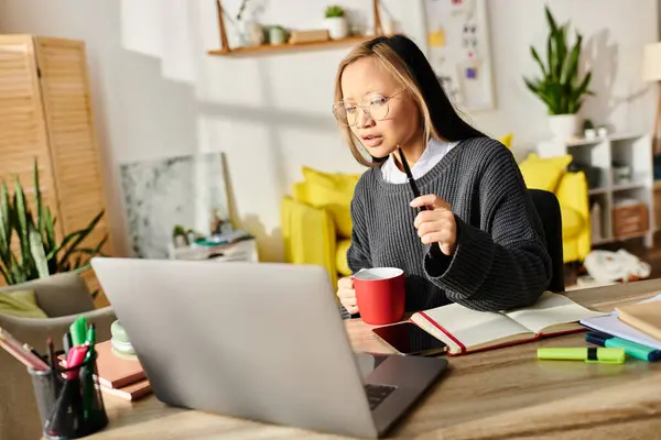 A focused young Asian woman immersed in her laptop, engaged in e-learning at home. — Stock Photo