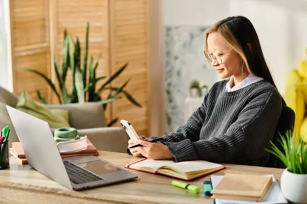 Une jeune femme asiatique concentrée sur son écran d'ordinateur portable, étudiant avec diligence à son bureau dans un environnement familial. — Photo de stock