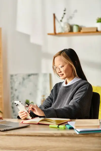 Une jeune femme asiatique assise à un bureau, engagée dans l'apprentissage en ligne sur son téléphone portable. — Photo de stock