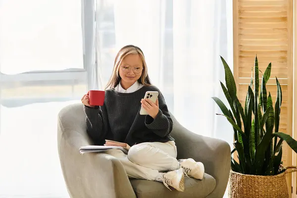 A young Asian girl studying at home, taking a break in a chair while holding a cup of coffee. — Stock Photo