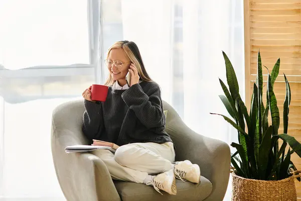 Uma jovem mulher asiática senta-se pacificamente em uma cadeira, livro aberto na frente dela, desfrutando de uma xícara quente de café. — Fotografia de Stock
