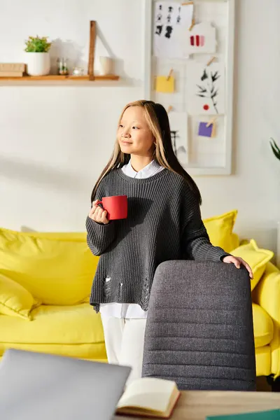 Uma jovem mulher asiática desfruta de um momento de paz em sua sala de estar iluminada pelo sol, segurando uma xícara de café. — Fotografia de Stock