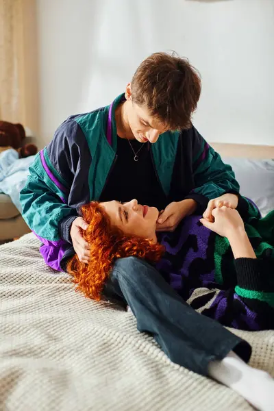 Amando boa aparência jovem casal em trajes acolhedores abraçando calorosamente enquanto deitado na cama em sua casa — Fotografia de Stock