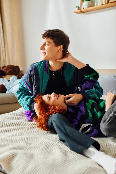 Seductora mujer alegre con el pelo rojo acostado en la cama con su novio alegre guapo mientras que en casa - foto de stock