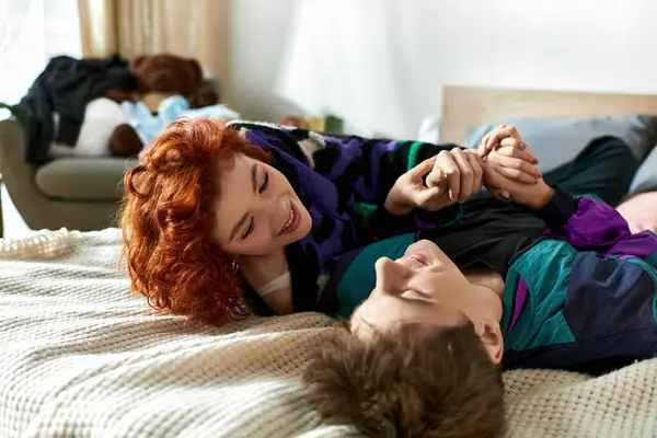 Atractiva pareja alegre en ropa vibrante pasar un buen rato juntos mientras se relaja en la cama - foto de stock