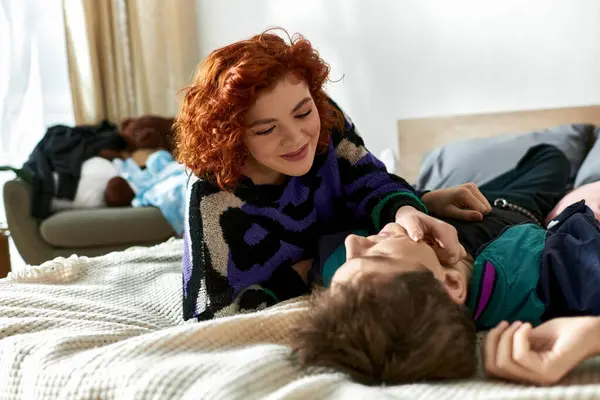 Belle femme aux cheveux rouges en tenue vive passer du temps avec son petit ami joyeux pendant qu'elle est au lit — Photo de stock