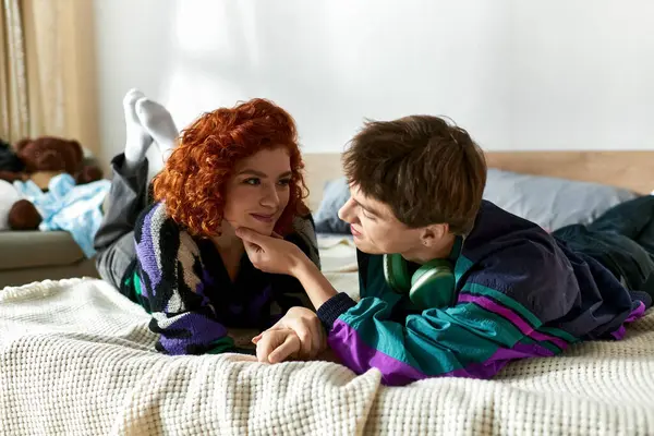 Alluring stylish couple in vibrant casual clothes lying in bed together and having great time — Stock Photo